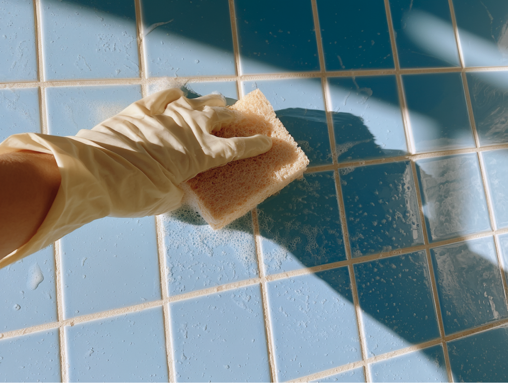 Gloved hand cleaning bathroom tile